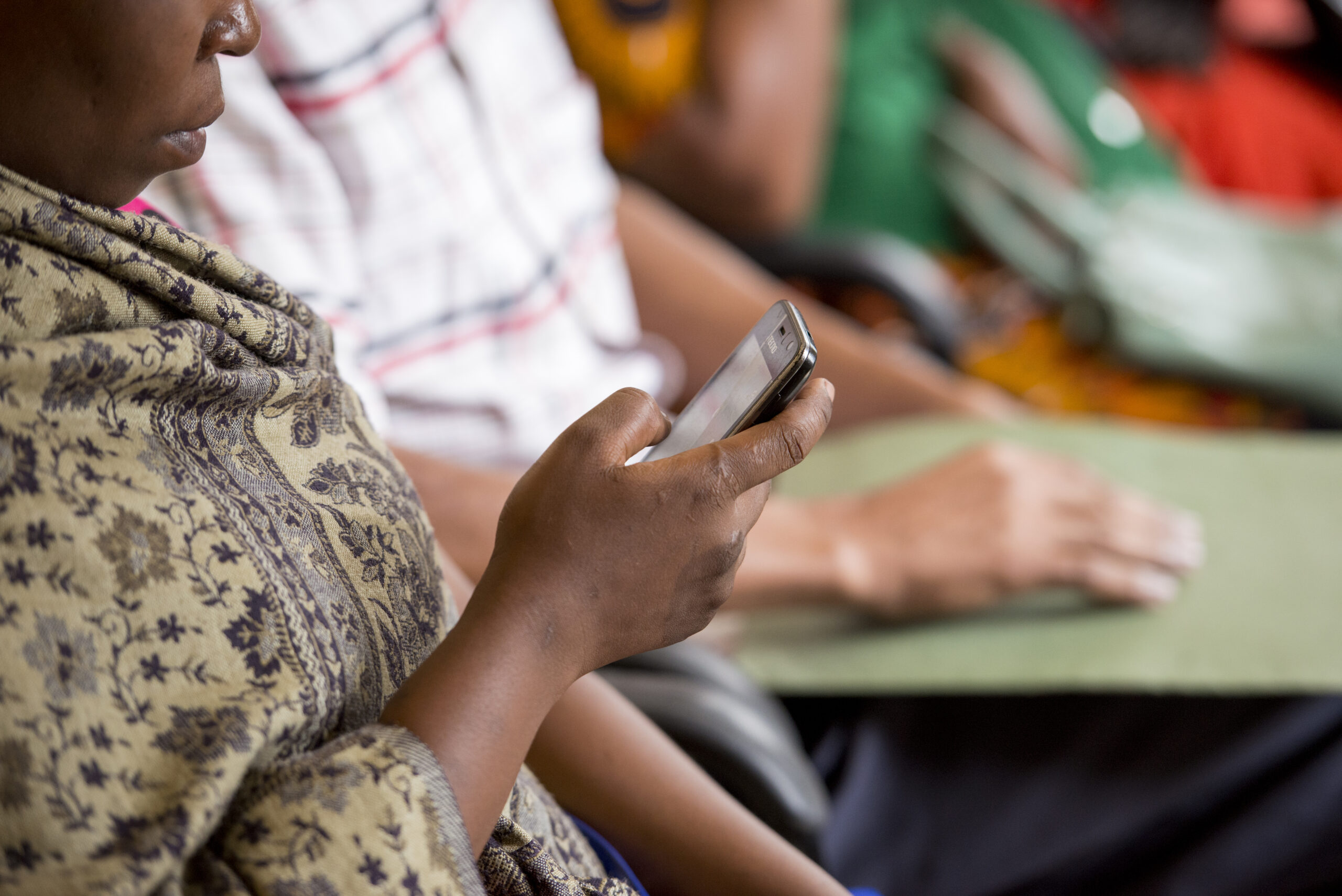 A woman looks at a mobile phone while seated with others during a community health meeting.