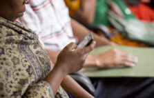 A woman looks at a mobile phone while seated with others during a community health meeting.