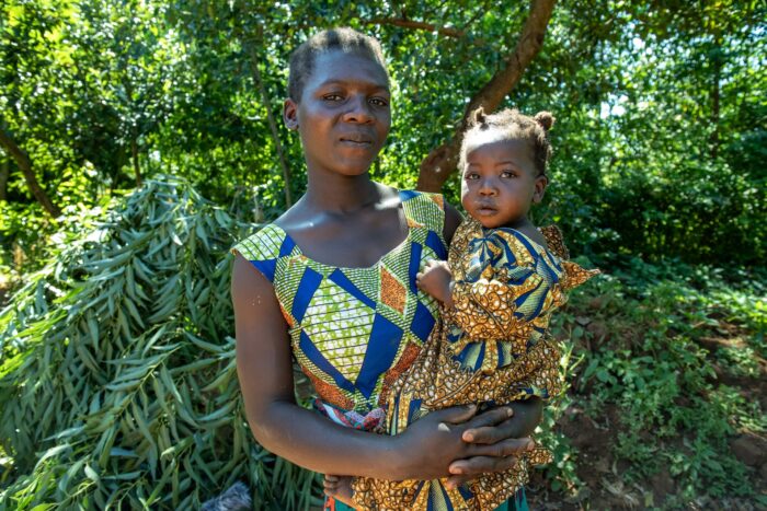 Mother holds her two year-old daughter and looks at the camera.