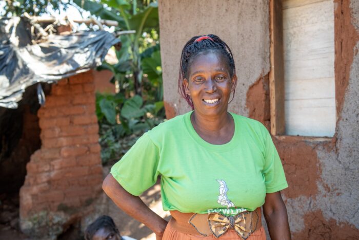 Mentor mother poses in front of a house in Malawi.